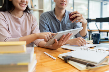 Fototapeta premium Two Asian students learning together with a laptop and tutor together at cafe