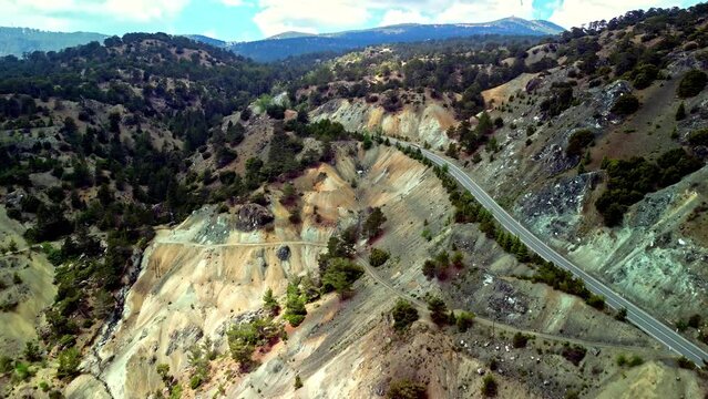 Drone view of Pano Amiantos, a former asbestos mine location. Beautiful mountain views with a single road winding through with many trees and mountains in the background.