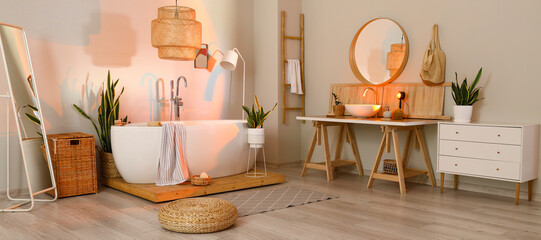 Interior of light bathroom with bathtub, table, sink and houseplants