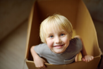 Cute preschool boy playing in a cardboard box during family's move to a new home. Kids play is a way of development of creative abilities.