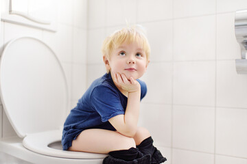 Cute little boy in restroom. Toddler child is training use toilet. Treatment of constipation of little kids. Teaching children of hygiene - obrazy, fototapety, plakaty