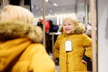 Cute little boy trying new coat during shopping. Fashion warm clothes for fall or winter. Child is...