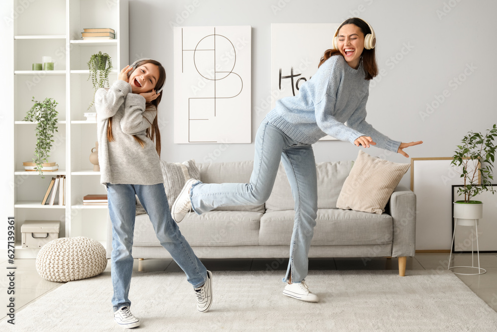 Wall mural Little girl and her mother in sweaters and headphones dancing at home