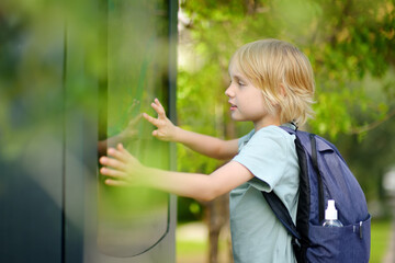 Little boy tourist studying at the big public outdoor street map of city. Kid touching screen and looking for the way. Child is interested in a visual map or advertising billboards on the street