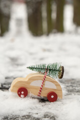 Wooden car carrying Christmas tree over snow. Copy space for text Toy car in snowy landscape. Merry...
