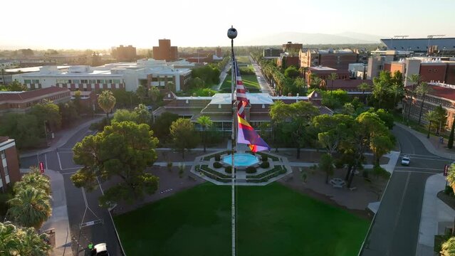 American flag and Arizona state flag in front of Old Main at University of Arizona campus. Aerial establishing dolly forward shot at sunrise.