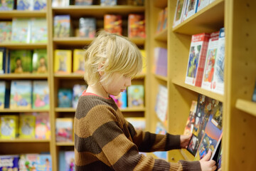 A preteen boy leafing through a book while standing at a bookshelf in a school library or bookstore.