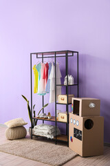 Shelving unit with children's dresses and shoes near lilac wall in room