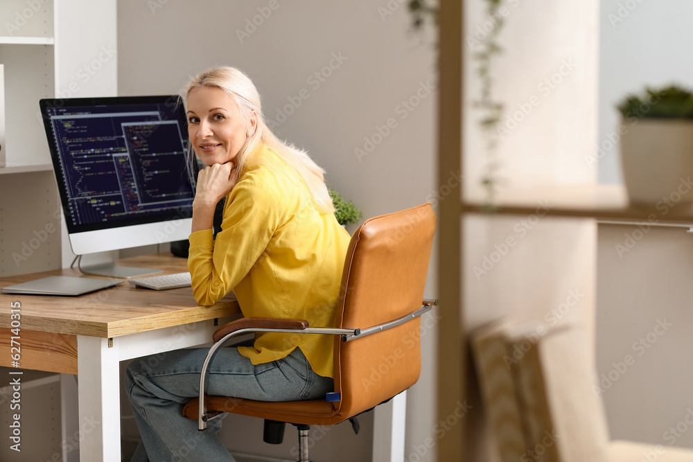 Wall mural mature female programmer working with computer at table in office