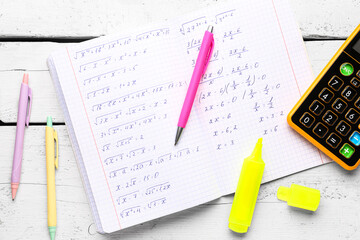Copybook with maths formulas, calculator and pens on white wooden table