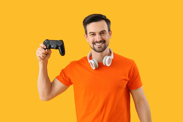 Fototapeta na wymiar Handsome man with game pad on yellow background