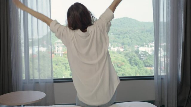 Asian beautiful woman lie down and jumping on bed at hotel, holiday vacation on summer day.