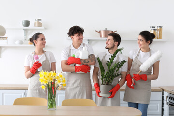Young janitors with cleaning supplies and houseplant in kitchen