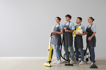 Young janitors with cleaning supplies near grey wall