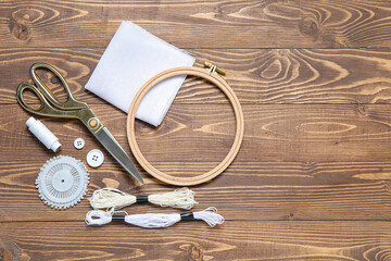 Embroidery hoop with canvas, scissors and mouline threads on brown wooden background © Pixel-Shot