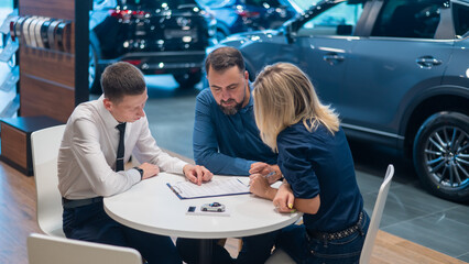 Happy caucasian couple signs a contract for the purchase of a car salon.
