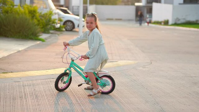 Ni&ntilde;a sola feliz rubia latina mexicana sonriente aprende a montar en bicicleta por las calles del vecindario en vacaciones en un caluroso verano al atardecer al aire libre soleado
