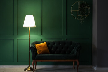 Glowing stand lamp with sofa near green wall in dark room