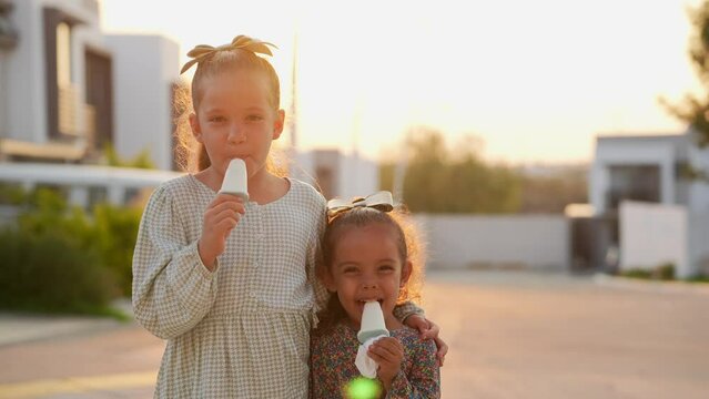 Dos ni&ntilde;as hermanas amigas primas latinas mexicanas hispanas comiendo y disfrutando de un rico helado una deliciosa nieve y paleta en la calle durante el caluroso verano en el atardecer al aire libre