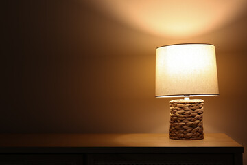 Glowing lamp on wooden table in dark room