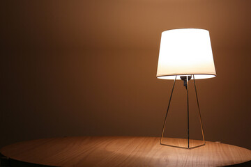 Glowing lamp on wooden table in dark room