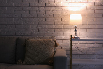 Glowing lamp on shelving unit near grey sofa in dark room
