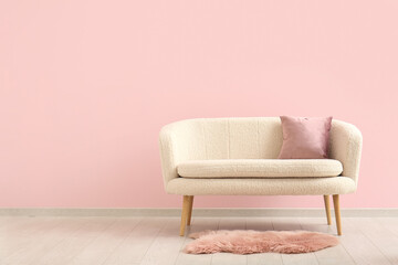 Cozy sofa with cushion and fur rug near pink wall