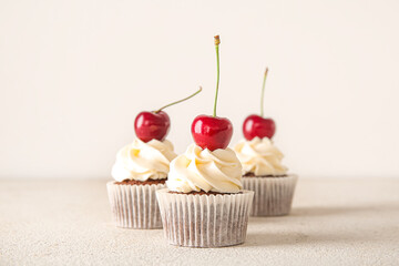 Tasty cherry cupcakes on light background