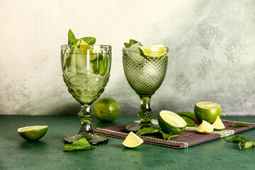 Glasses of cold mojito, mint leaves and limes on color table against light wall