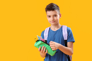 Little schoolboy with pencil case on orange background