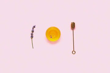 Glass bowl of sweet lavender honey and dipper on pink background
