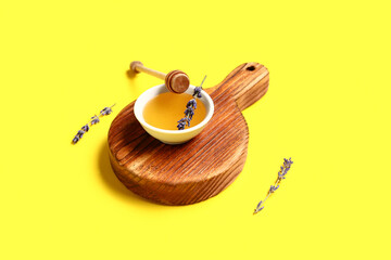 Wooden board with bowl of sweet lavender honey, dipper and flowers on yellow background