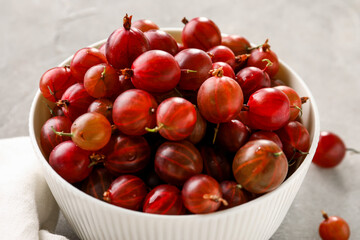Bowl with fresh gooseberries on grey background