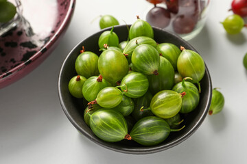 Bowl with fresh gooseberries on white background