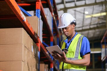 Man american african professional worker wearing safety uniform and hard hat using digital tablet inspect product on shelves in warehouse.