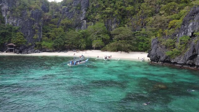 Island Hopping Boats and people snorkeling in tropical clear blue water of Serenity Beach on Cadlao Island in El Nido, Philippines. Aerial