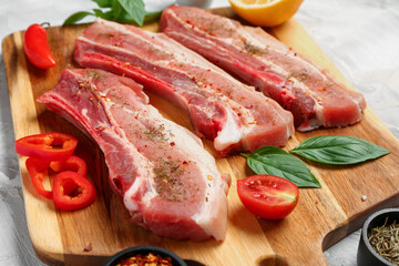 Wooden board with raw pork ribs and spices on grunge background, closeup