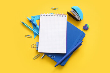 Composition with blank notebook and school stationery on yellow background