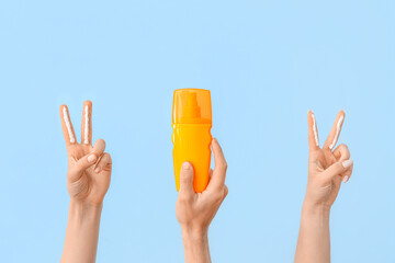 Female hands with bottle of sunscreen cream showing victory gesture on blue background