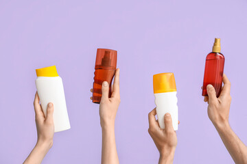 Female hands with bottles of sunscreen cream on lilac background