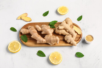 Wooden board with fresh ginger roots and slices of lemon on white background