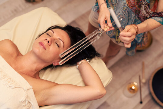 Young woman getting treatment. Sound massage and sound healing. Relax and therapy. Patient feeling calm and zen from massage and holistic medicine.