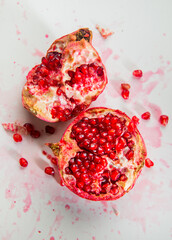Smashed opened juicy pomegranate fruit on white background. Food photography with fresh and juicy pomegranate with red arils or seeds.