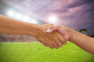 handshake in a business opponent team players shaking hand on football stadium background