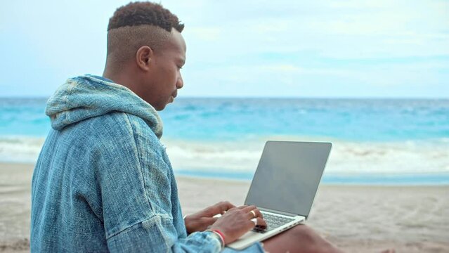 Male freelancer work near ocean. African american guy use macbook laptop. Black person rest open air. Afro man typing computer. Sea beach view. Marine shore. Focused outdoor job. Happy digital nomad.
