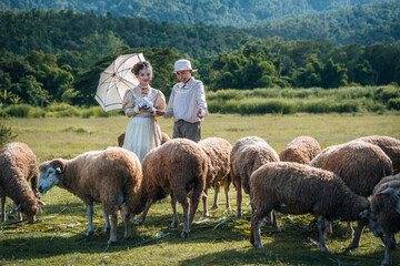 Obraz premium teenage girl and boy in ancient-style costumes holding an umbrella happy together in the sheep pasture. vintage blouse costume. Historical dresses, victorian or edwardian era style dress
