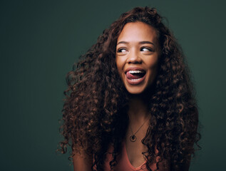 Natural beauty, tongue out and happy gen z girl with hair, curly and curious on green background. Afro, wellness care and female model with fun, emoji and silly face, personality or comic in studio