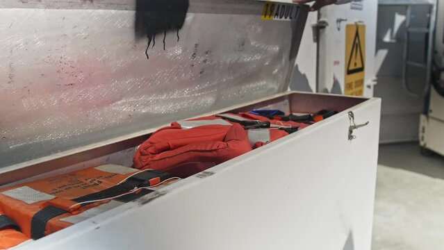 A man opens a life jacket trunk on a boat and takes one out to put on.