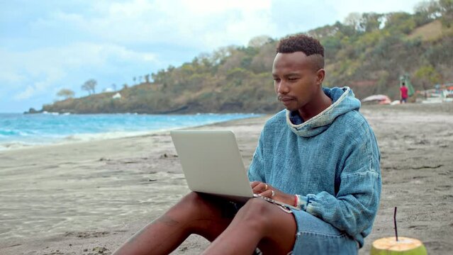Male freelancer work near ocean. African american guy use macbook laptop. Black person rest open air. Afro man typing computer. Sea beach view. Marine shore. Focused outdoor job. Happy digital nomad.
