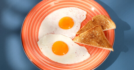fried eggs with toast on a red plate. close-up. angle view. camera tracking. blue background. traditional breakfast. sunny day.